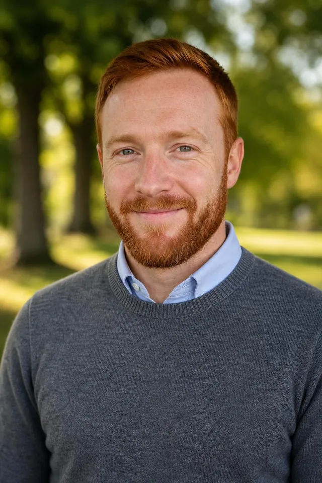 Man with a red beard in a grey sweater in a sunny park