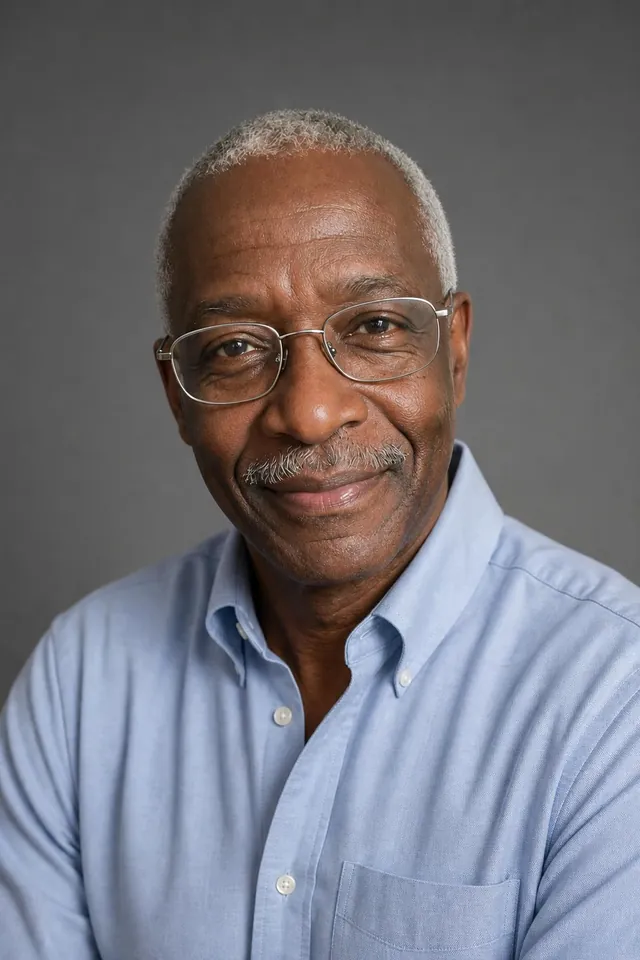 Older man with glasses in a light blue shirt on a grey studio backdrop