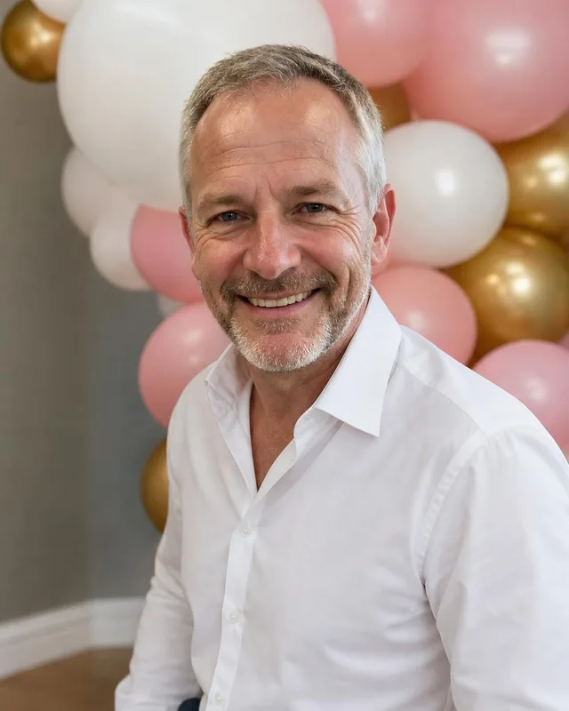 Man in a white shirt in front of pink, white and gold balloons