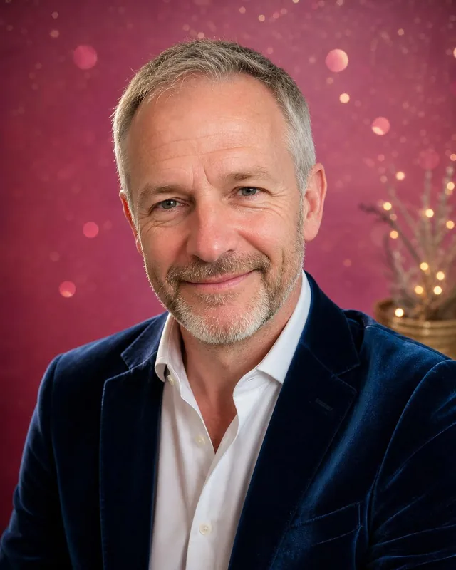 Man in a navy velvet blazer against a pink sparkle backdrop
