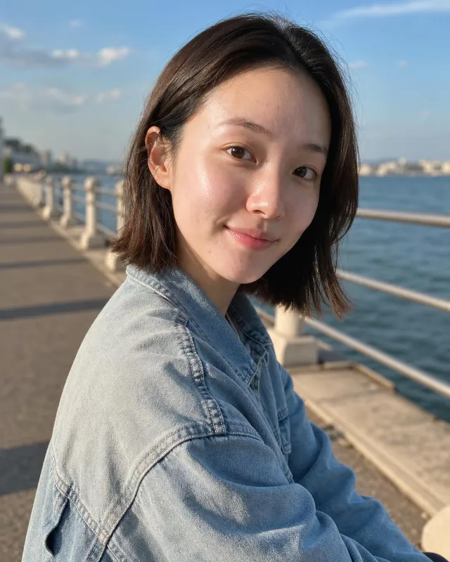 Woman in a denim jacket on a seaside promenade, looking back over her shoulder