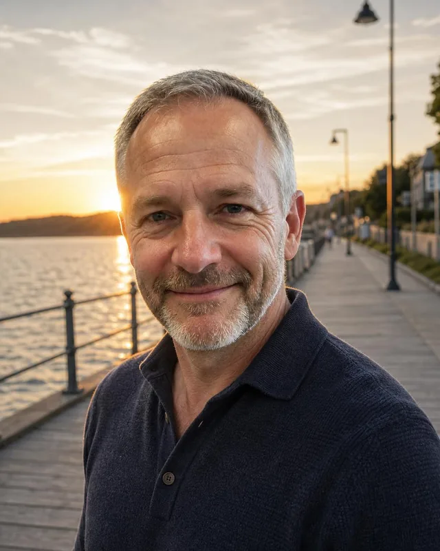 Man in a navy knit polo on a waterfront boardwalk at sunset