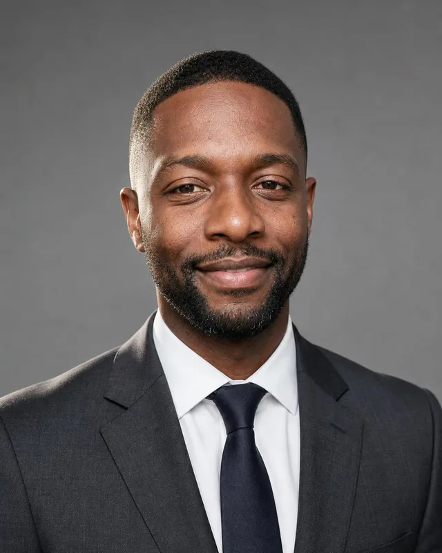 Doctor headshot: man in a charcoal suit and dark tie against a grey studio backdrop