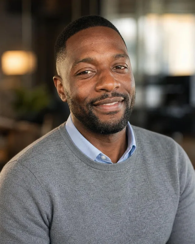 Man in a grey sweater over a blue collared shirt in a softly lit office